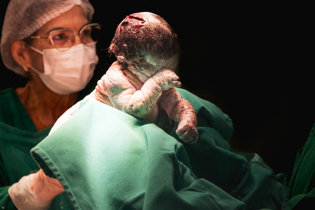 A newborn baby held by a nurse shortly after birth in a hospital setting.